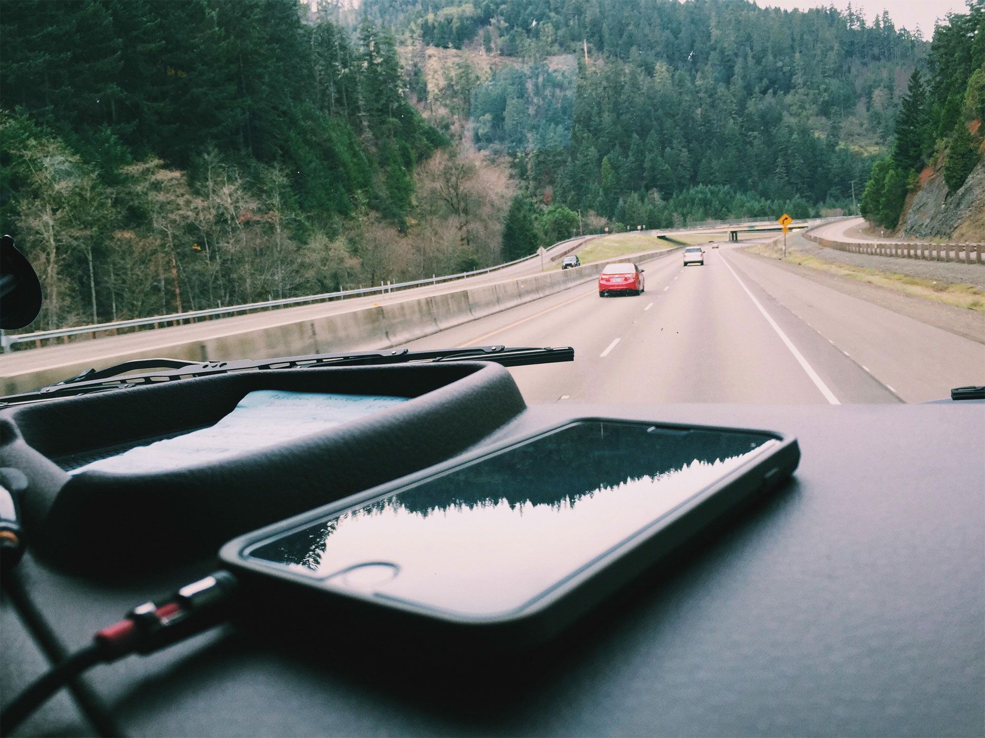 smartphone on dashboard with highway and trees in background
