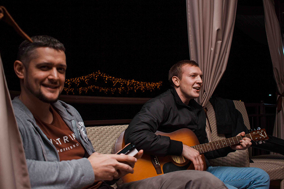 two men playing guitar and singing at an evening celebration