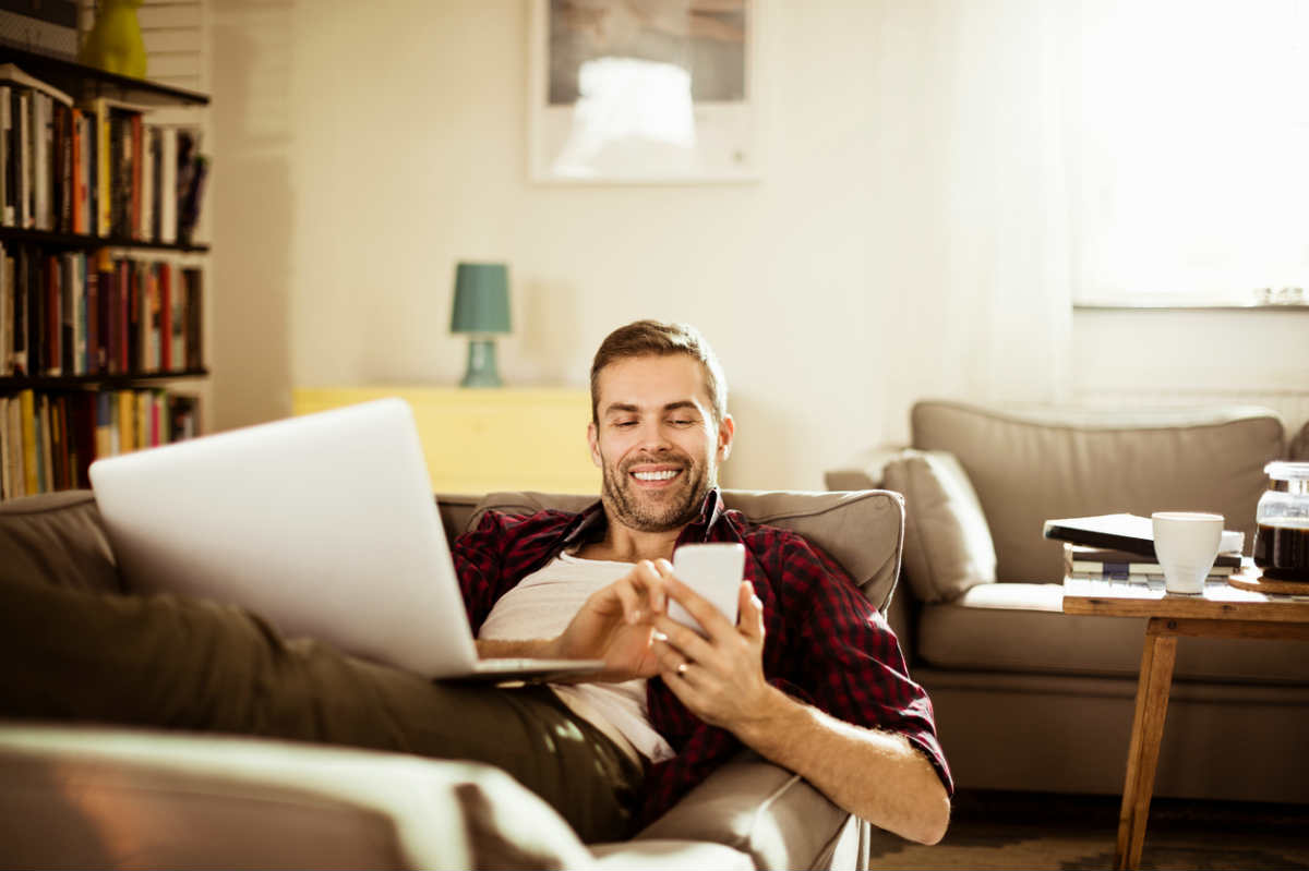 man using laptop and smartphone while relaxing on a couch