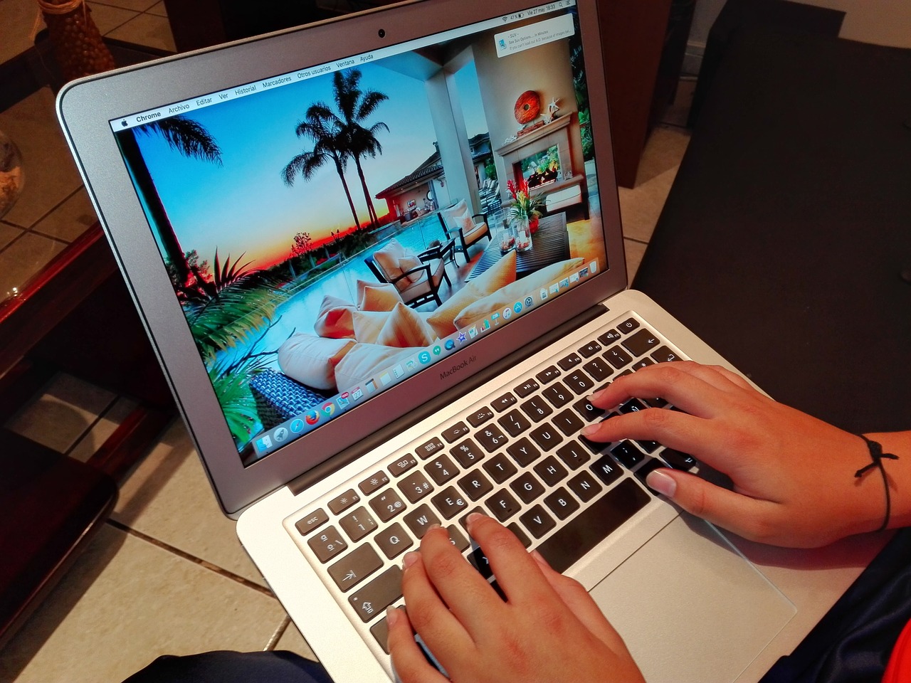 person typing on laptop with beach resort image on screen