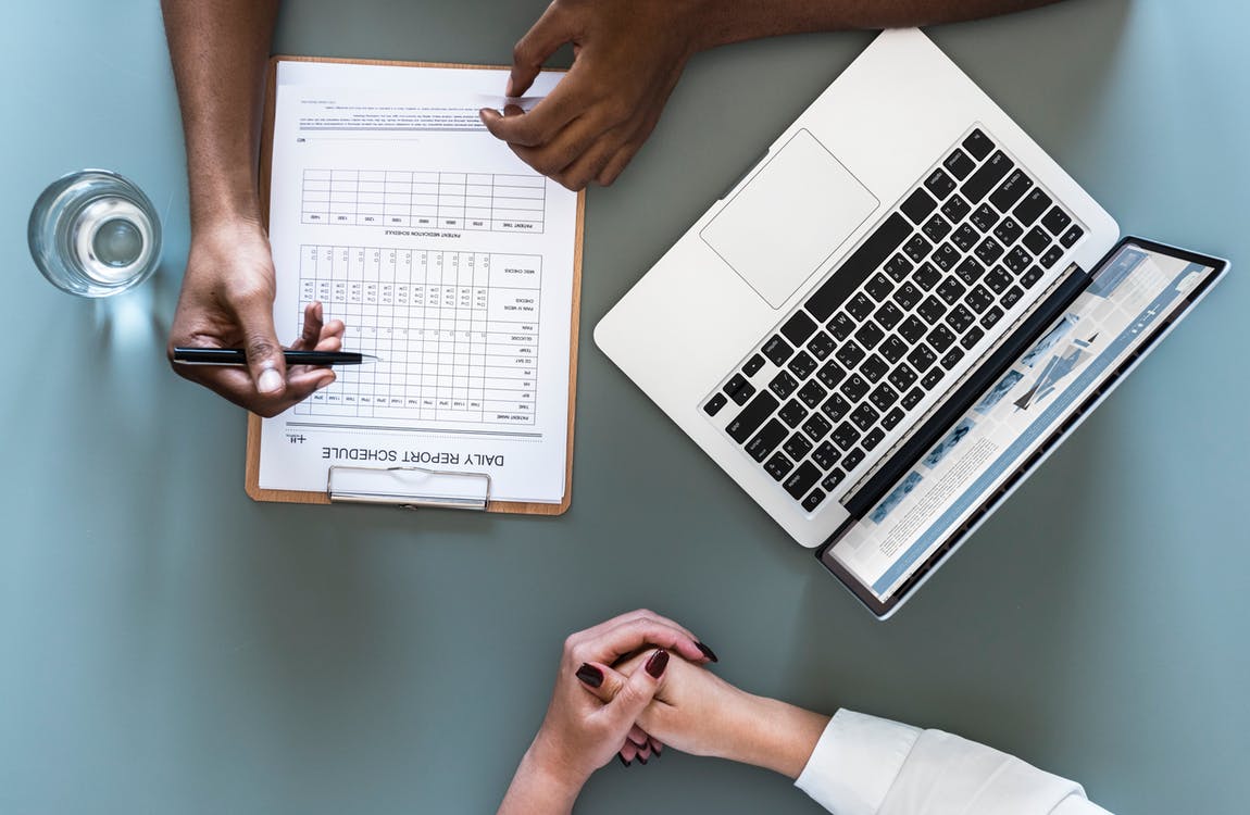 hands holding pens over a laptop and a scheduling document